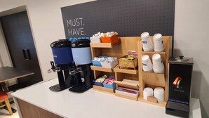 Eine Kaffeestation mit zwei Kaffeeautomaten, einer Auswahl an Kaffeekapseln und einem Warmwassergerät.