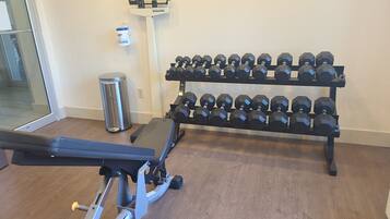 A gym with a bench press, a dumbbell rack, and a trash can.