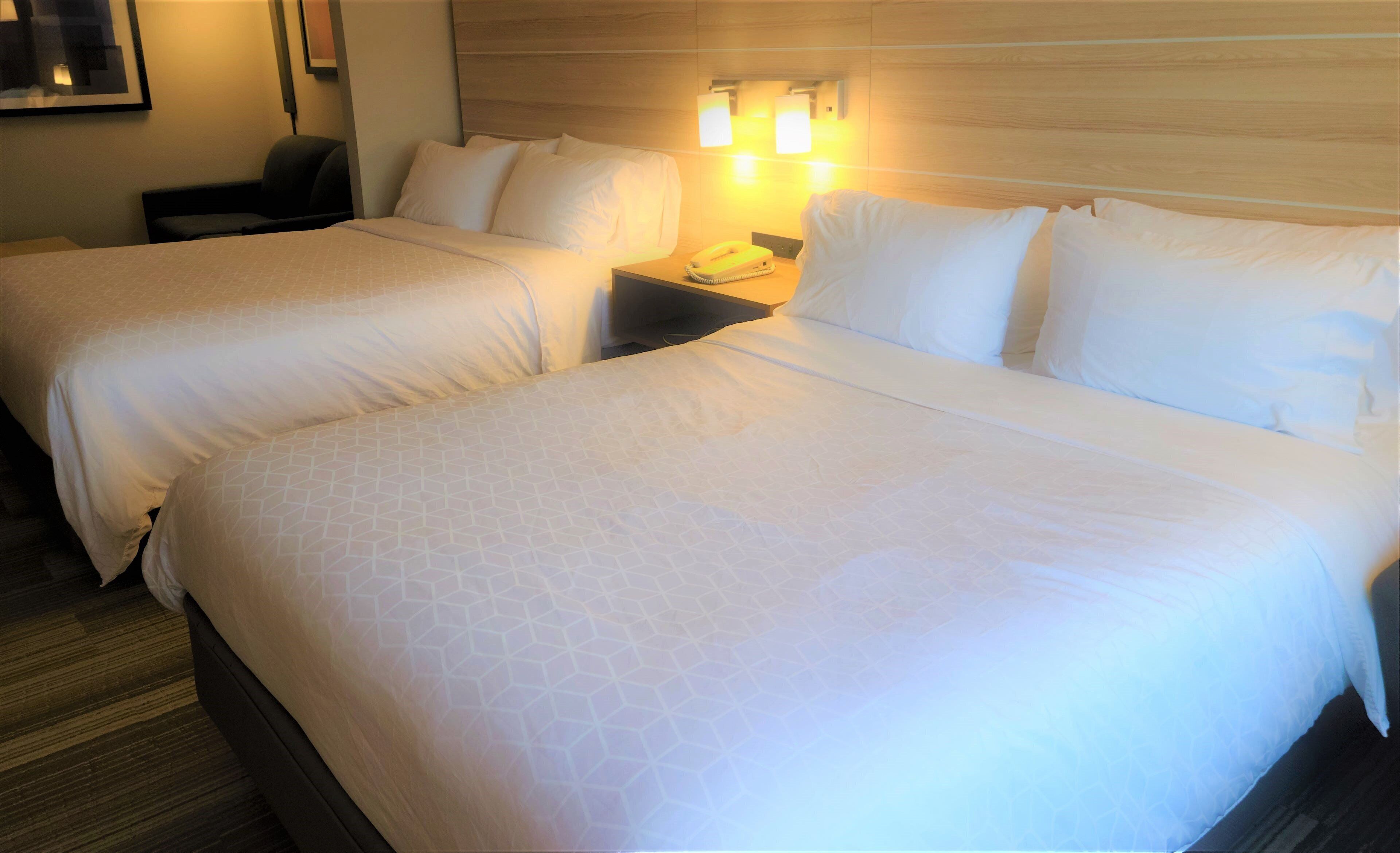 Una habitación de hotel con dos camas, una mesita de noche con teléfono e iluminación en la pared.