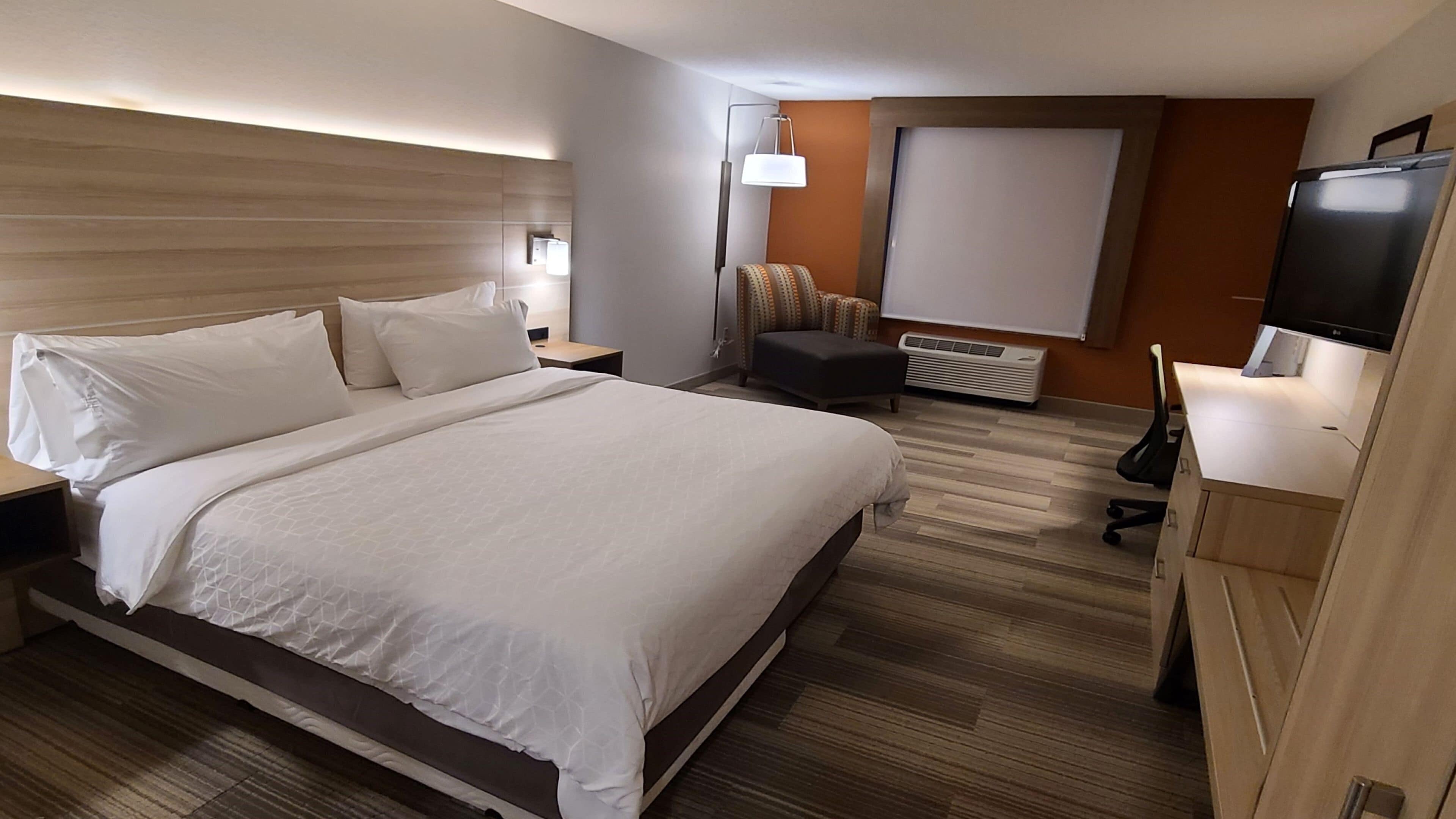 Habitación de hotel con una cama grande, un escritorio, una silla, un televisor y aire acondicionado instalado en la pared.