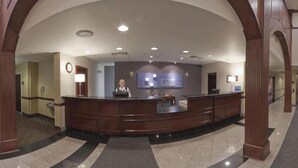 Un espace d’accueil d’hôtel comprenant un comptoir d’accueil incurvé, un réceptionniste et un bureau d’accueil.