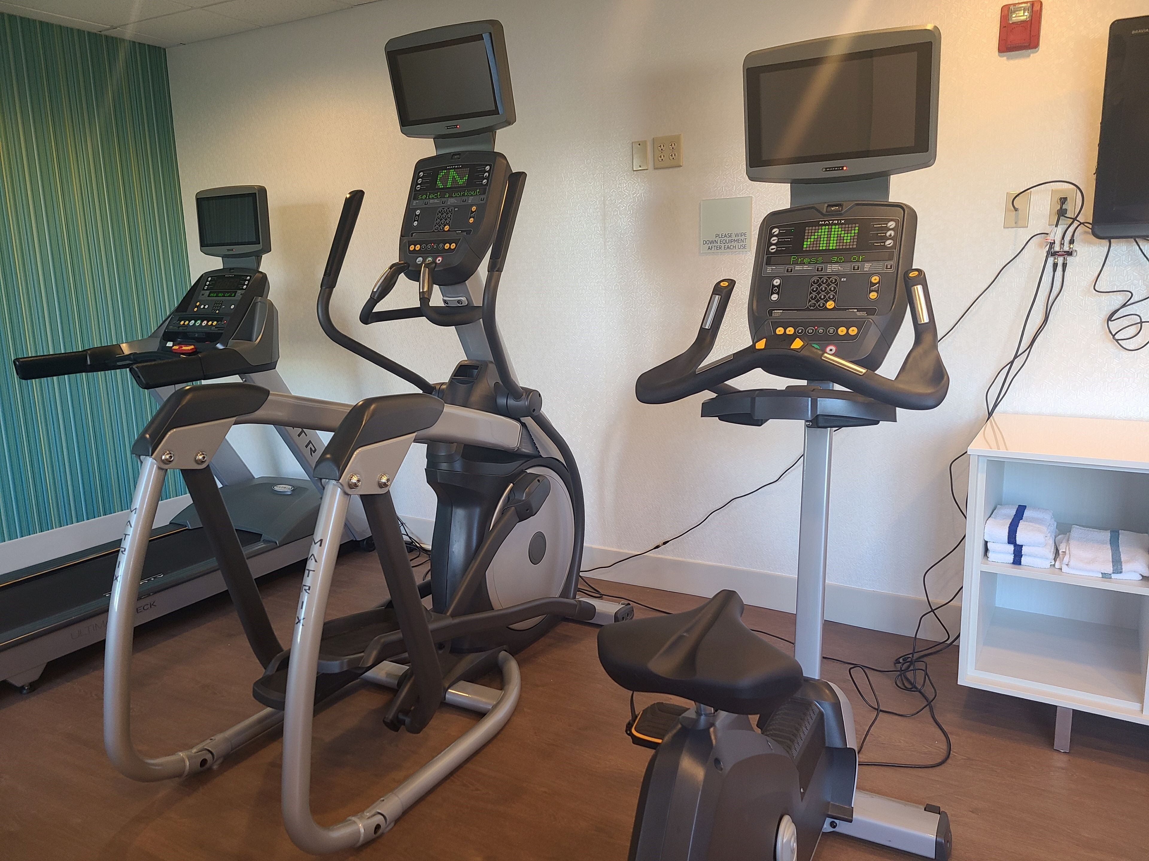 Three exercise bikes with digital displays, a treadmill, and a wall-mounted television.