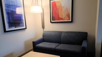 A room with a dark grey sofa, a small table, and two framed artworks on the wall.