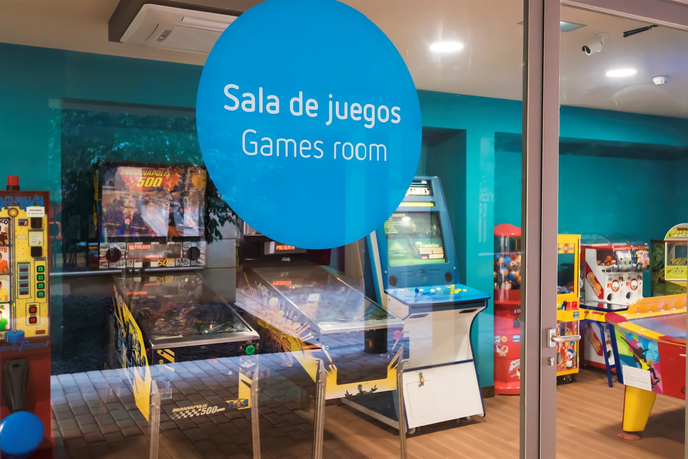 A games room with various arcade machines and a large blue sign indicating the room's name.