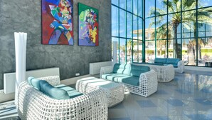 A modern lounge area with wicker furniture, large windows, and abstract art on the wall.