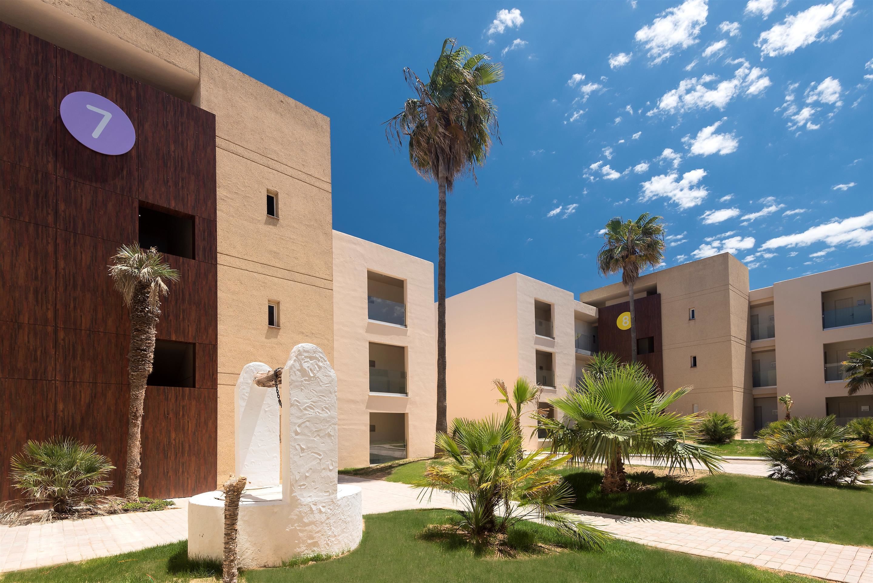 Un bâtiment moderne, orné d’un panneau portant le chiffre « 7 », entouré de palmiers et doté d’une pelouse bien entretenue.