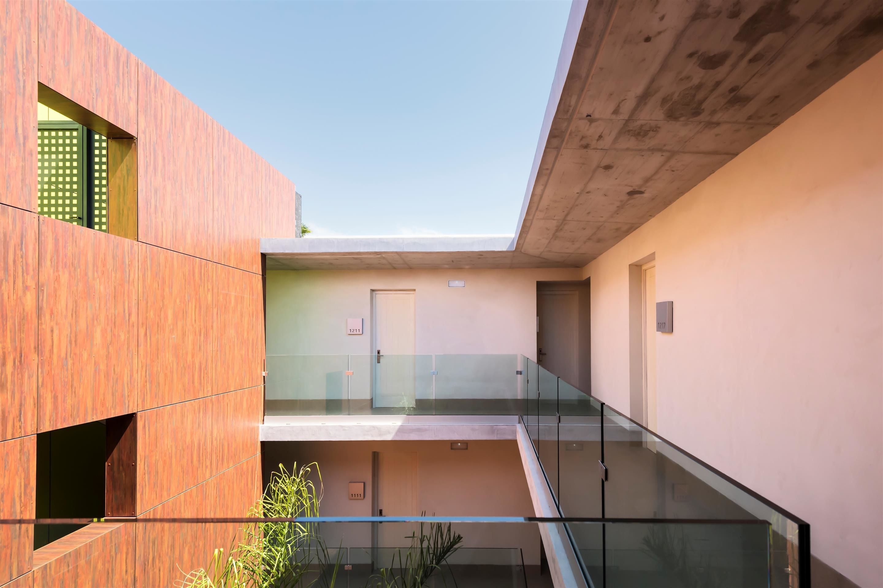 Un bâtiment moderne doté d’un balcon en verre, d’un plafond en béton et d’une porte avec une plaque numérotée.