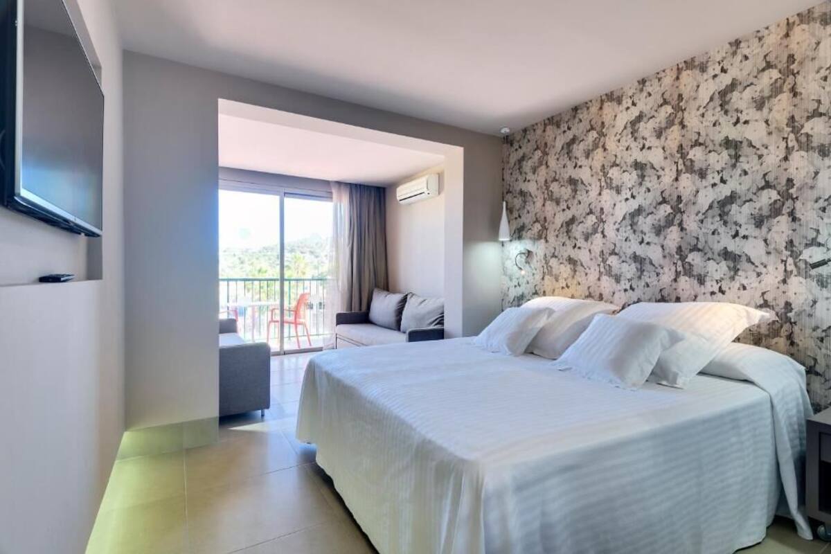 Une chambre d’hôtel avec un grand lit, un balcon avec une chaise et un téléviseur fixé au mur.