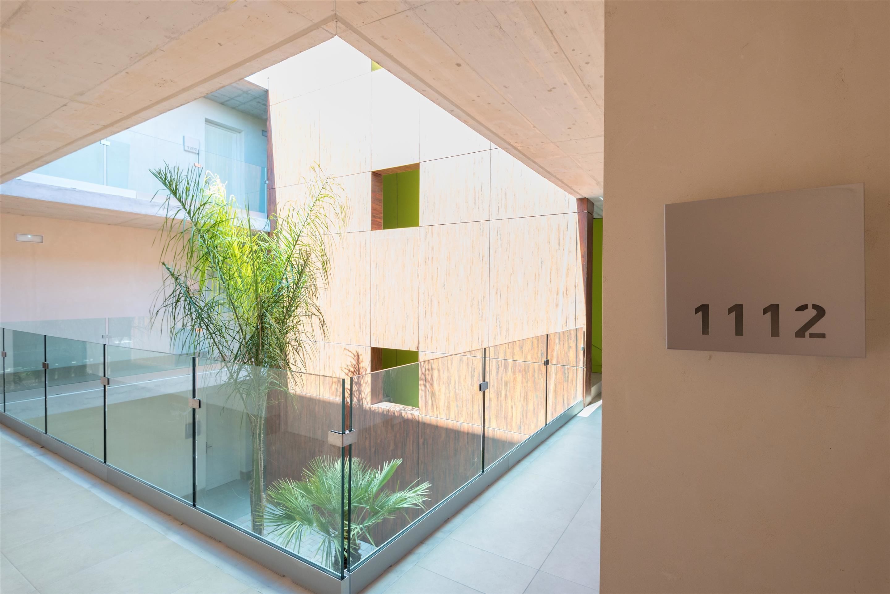 A modern interior with a glass railing, a potted plant, and a sign with the number 1112.