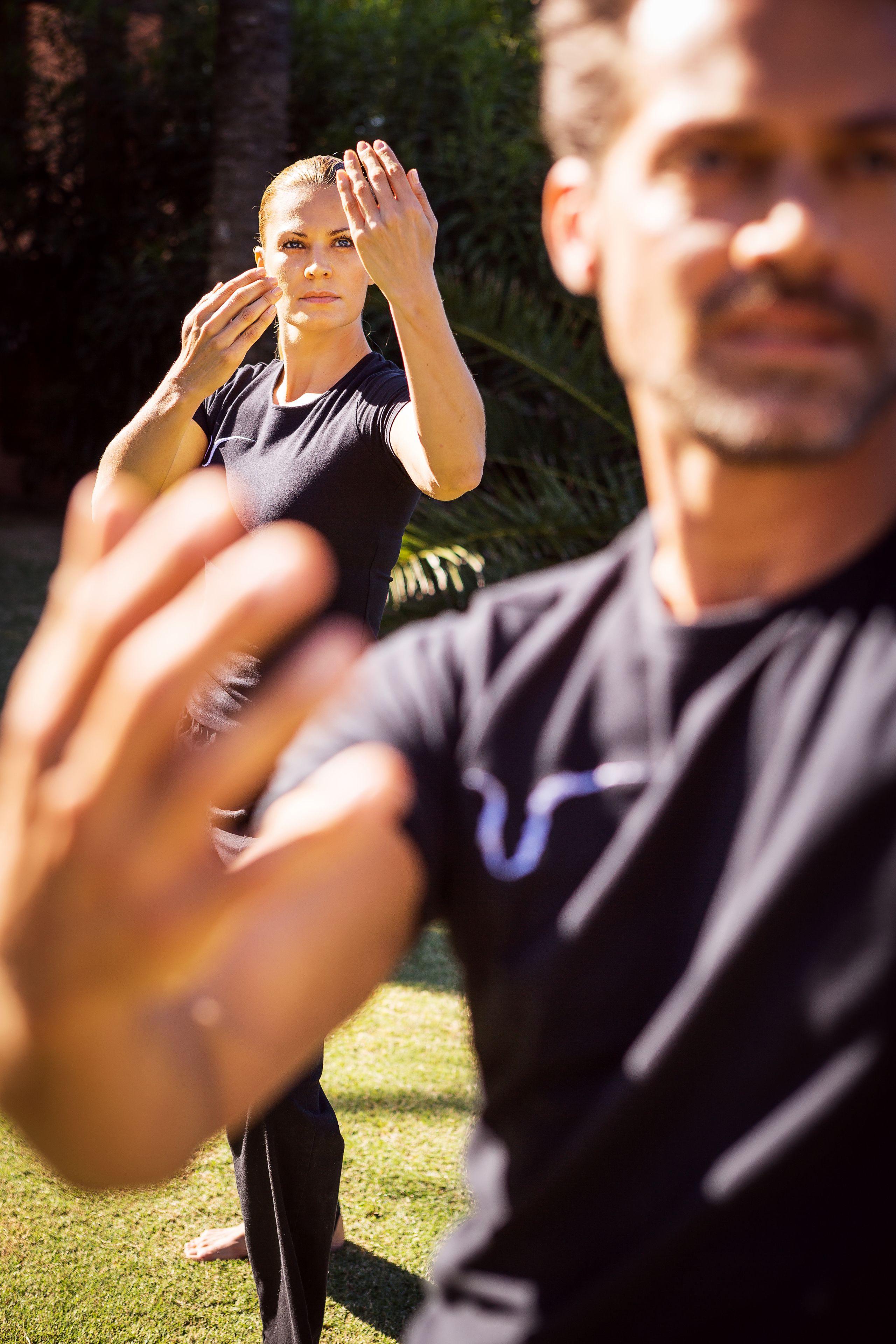 Une personne portant un t-shirt noir orné d’un logo, debout à l’extérieur, avec de la verdure en arrière-plan.