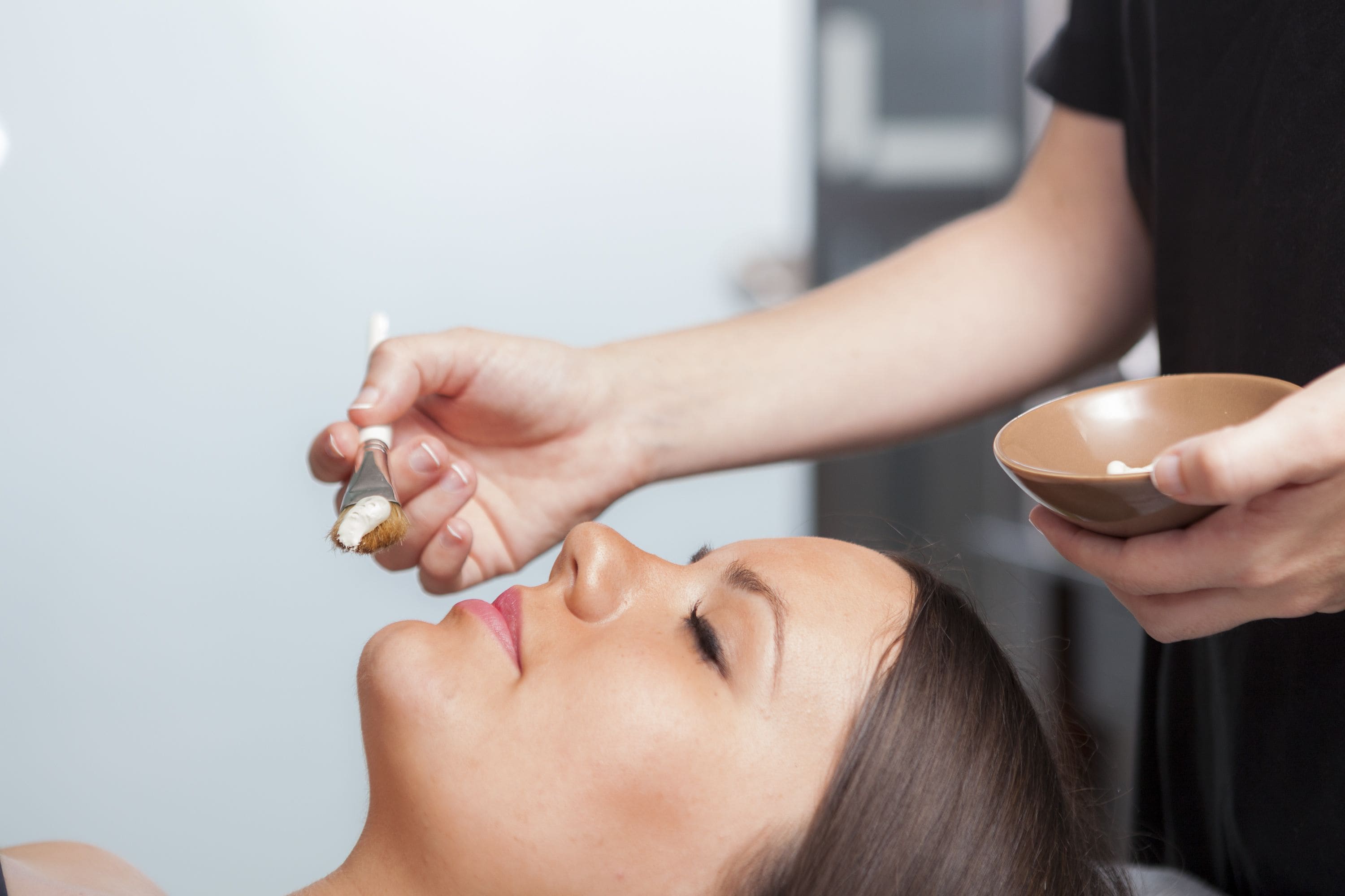 A person receiving a facial treatment with a brush and a bowl.
