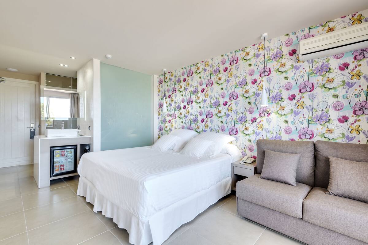 Une chambre comprenant un lit, un canapé, une petite table de chevet, un climatiseur fixé au mur et un mini-réfrigérateur.