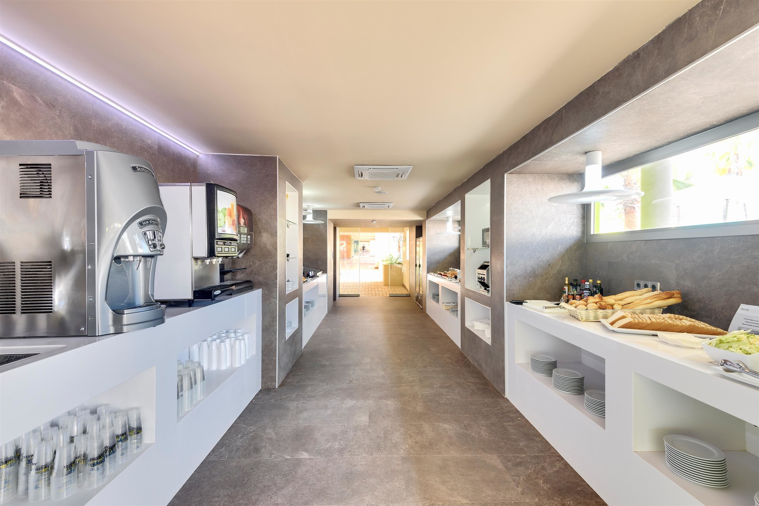 A modern kitchen area with a coffee machine, a display screen, and a variety of food items on shelves.