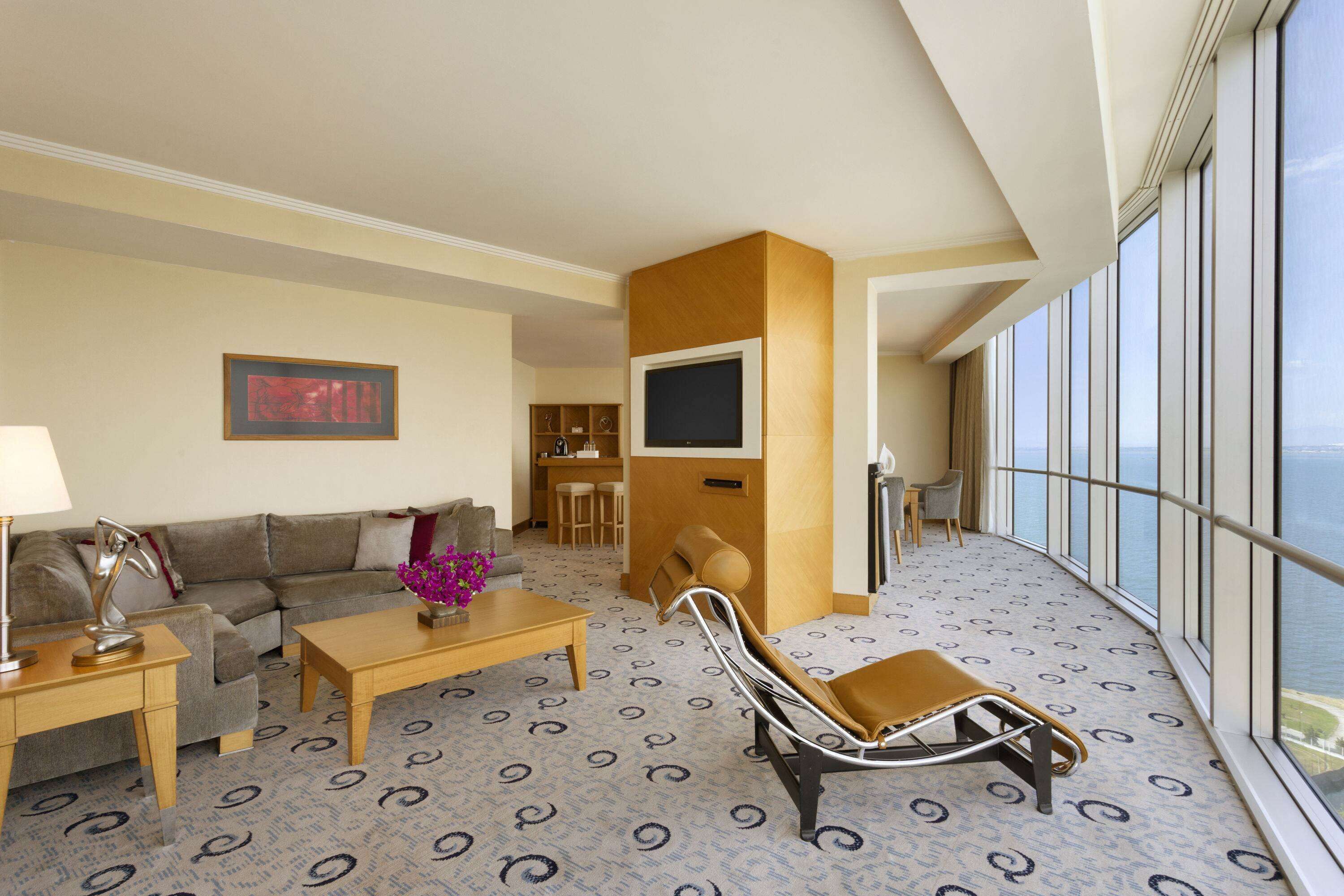 A hotel room with a sofa, a coffee table, a TV, and a balcony with a view.