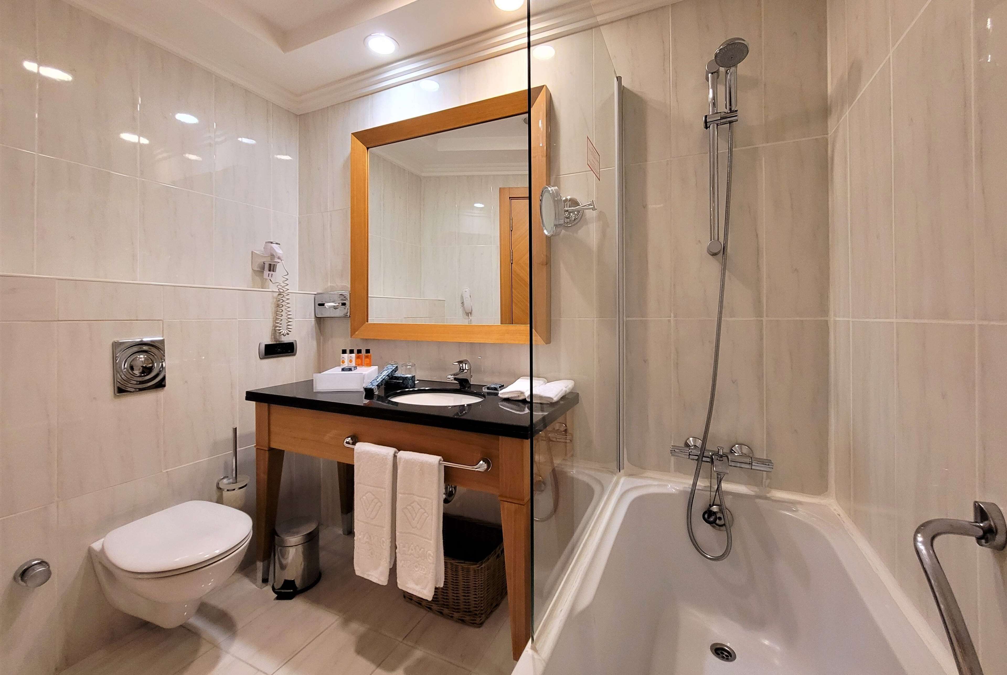 A modern bathroom with a glass-enclosed shower, a bathtub, a sink with a mirror above, and a toilet.