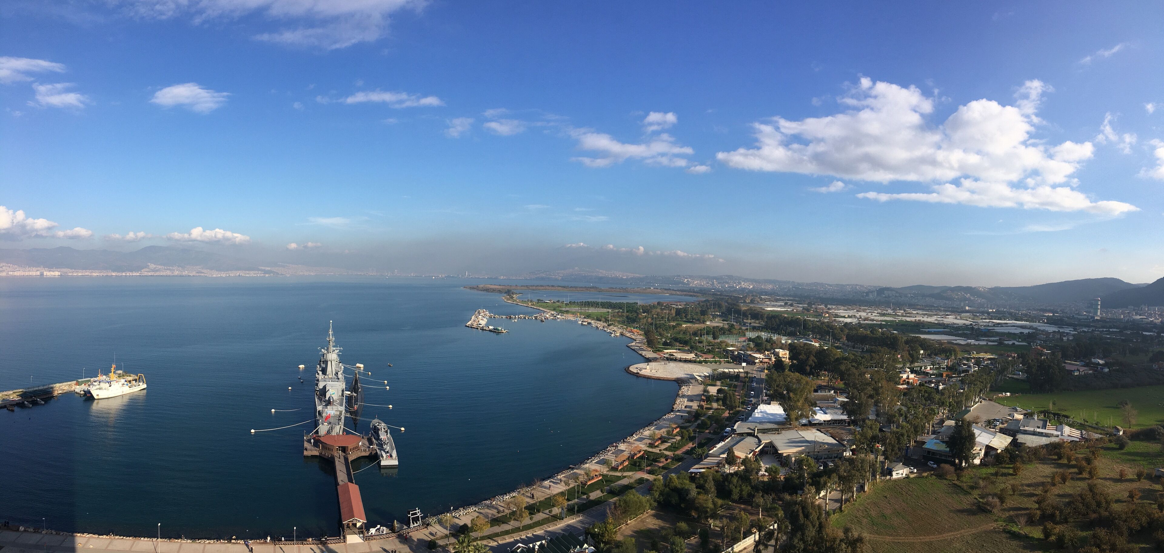 A coastal cityscape with a large ship docked at a pier, surrounded by residential areas and a clear sky.