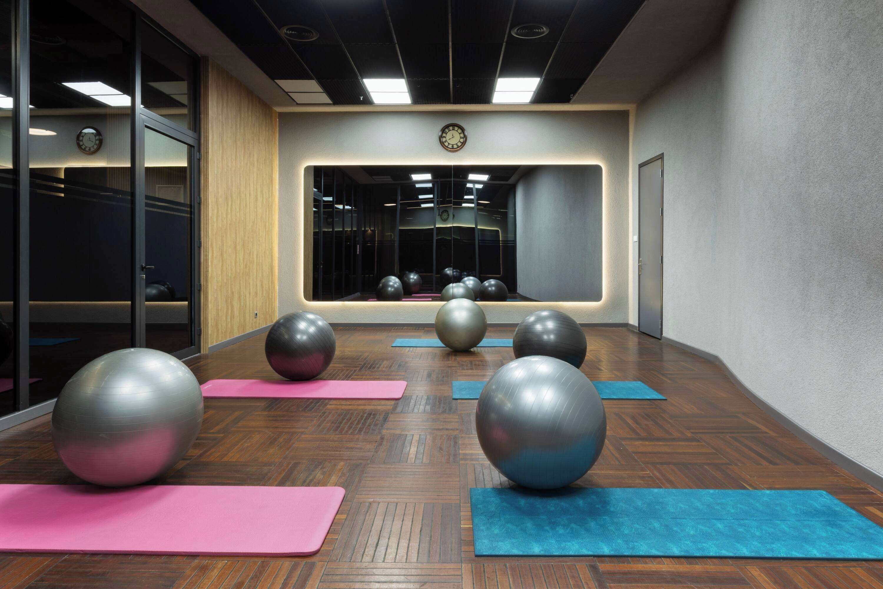 Ein Fitnessraum mit Übungsbällen und Matten, Holzböden und einem großen Spiegel.