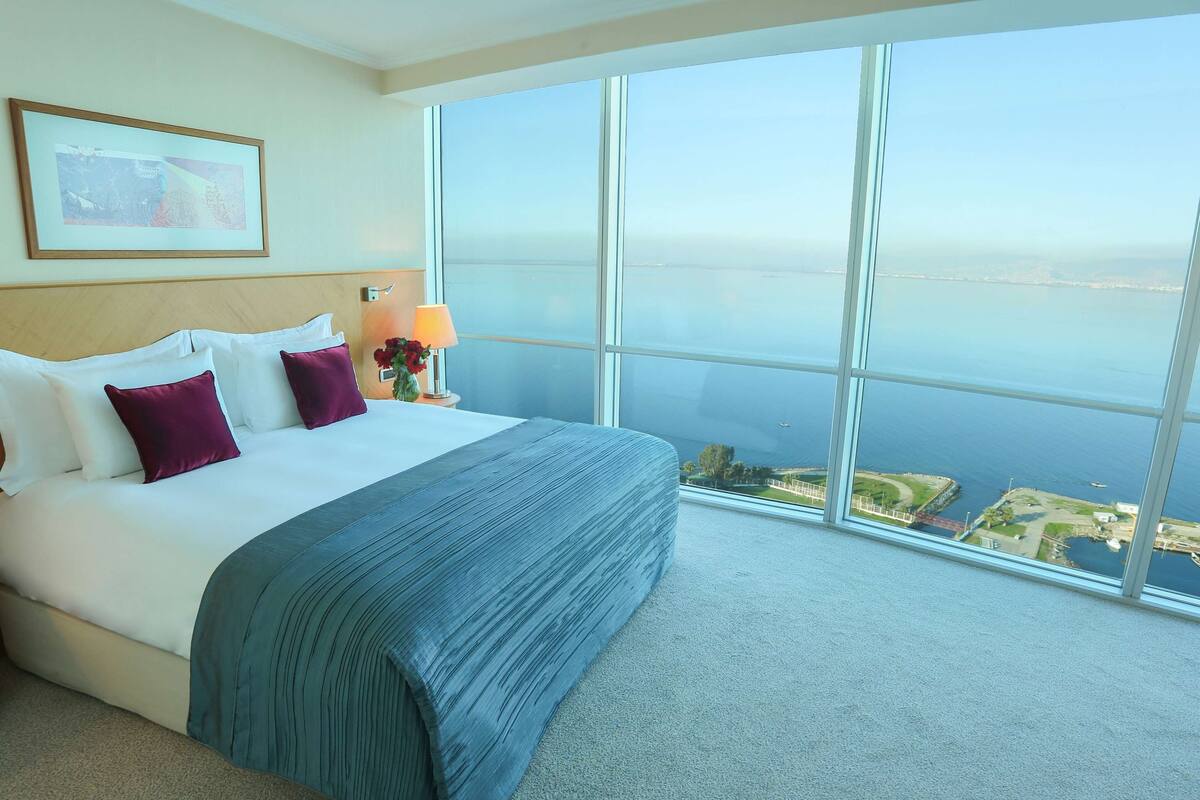 A hotel room with a large bed, a view of the sea, and a framed picture on the wall.