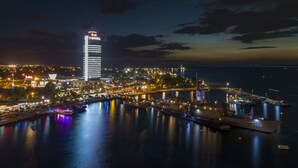 Een stadsgezicht aan het water in de nacht, met verlichte gebouwen, een jachthaven en een groot cruiseschip dat aanlegt.