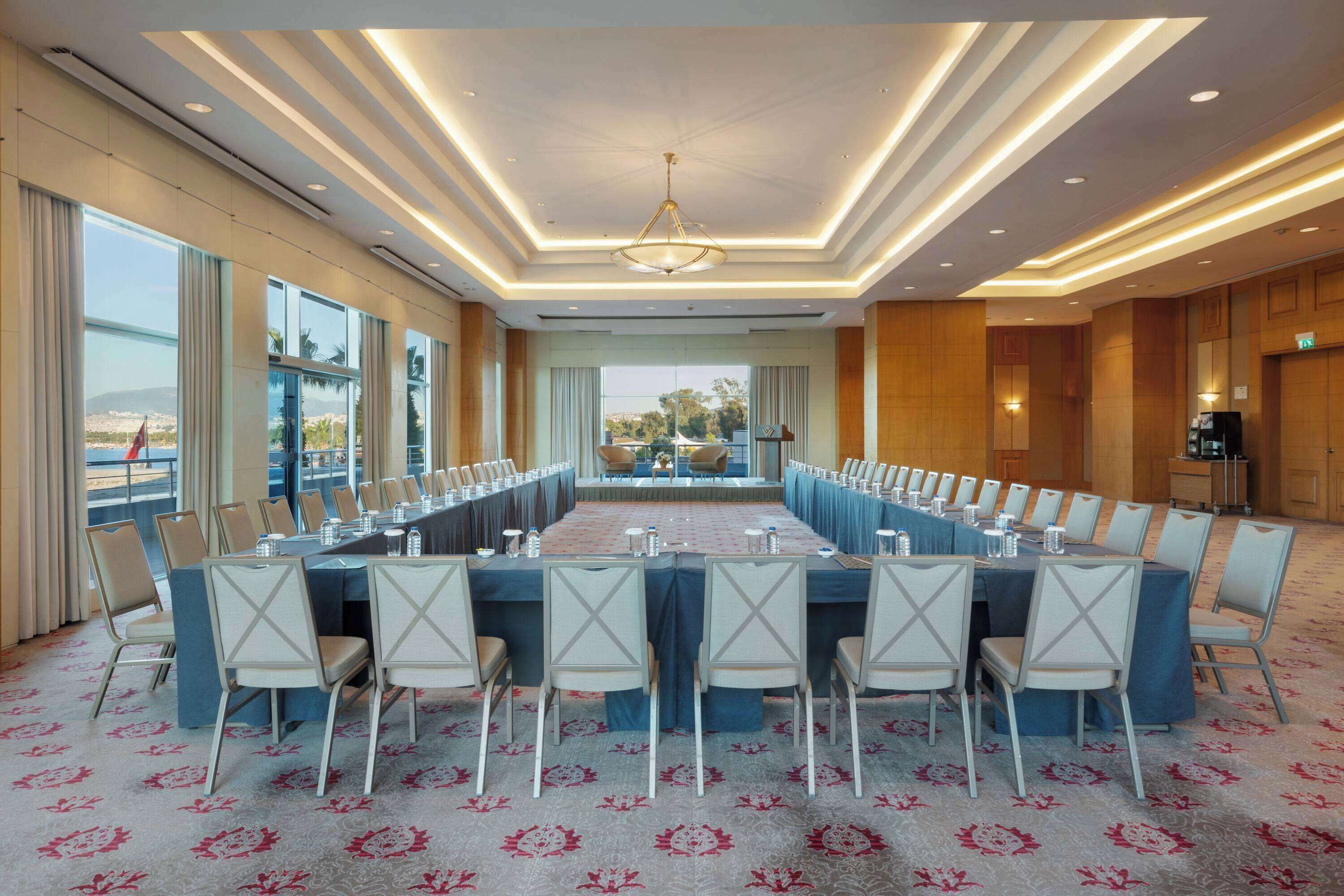 Un salón de conferencias con una larga mesa, sillas y vistas al exterior.