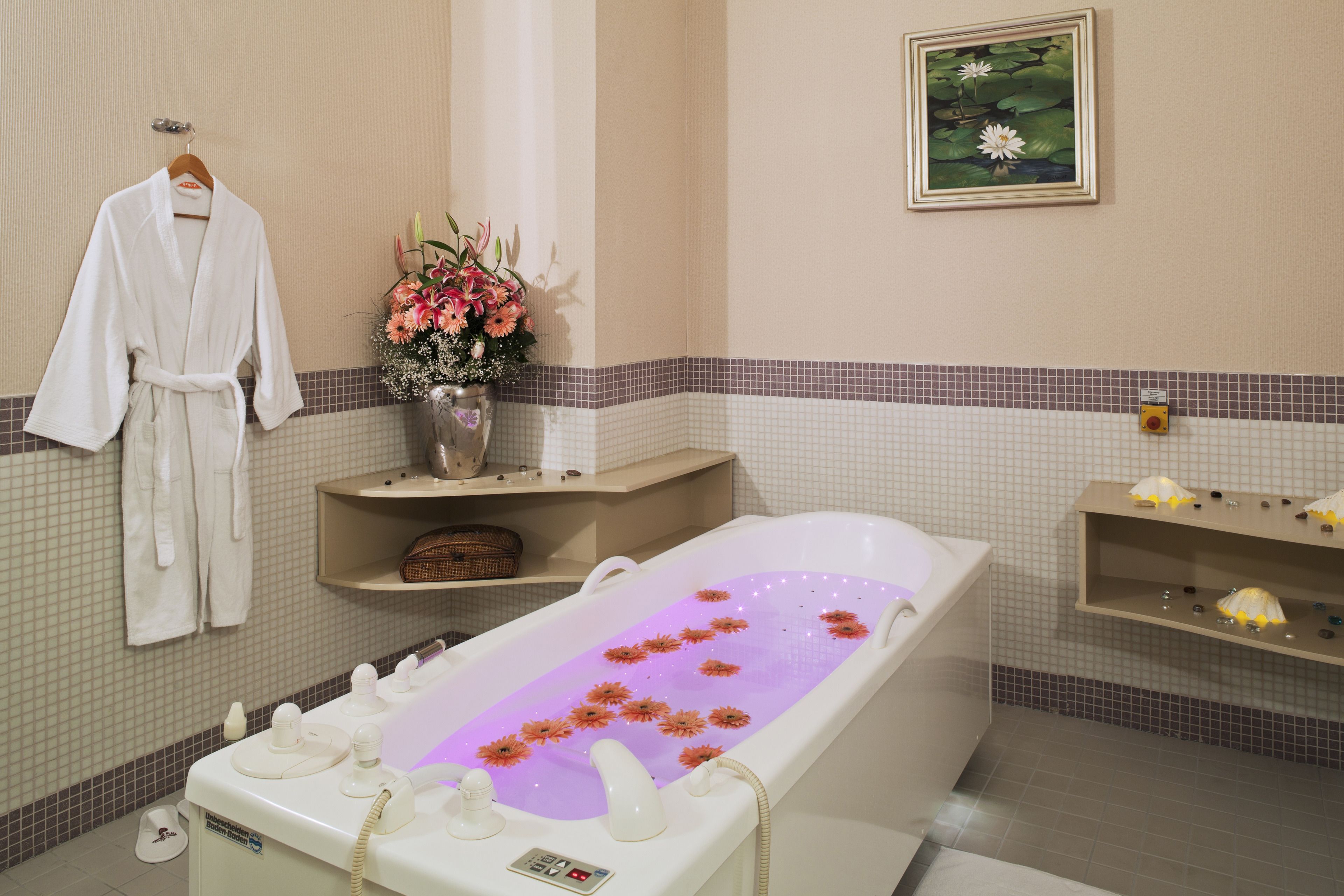 A bathroom with a bathtub filled with water and flowers, a white robe hanging on the wall, and a shelf with toiletries.