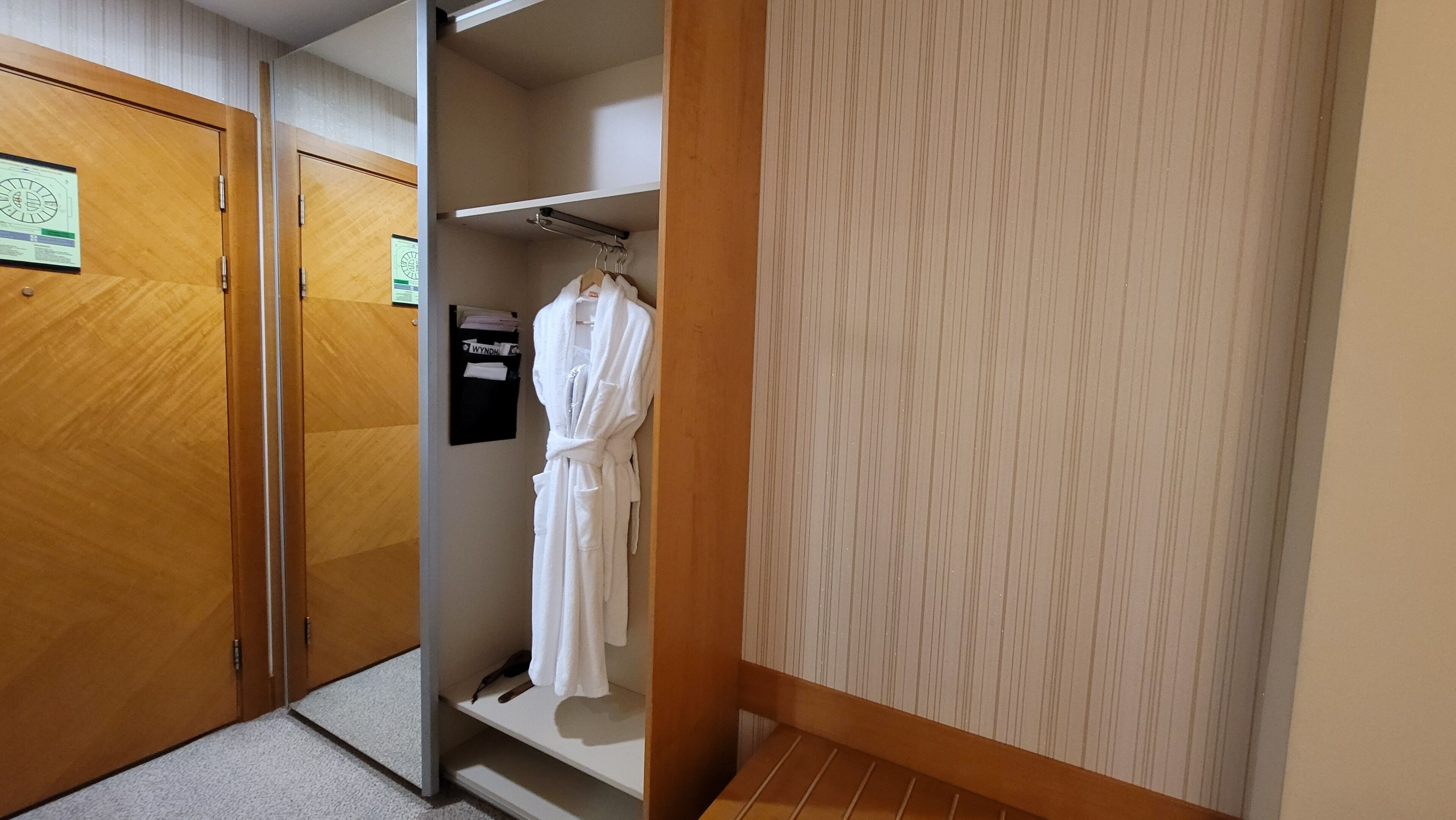 A hotel room with a wooden wardrobe, a robe hanging on a rack, and a small shelf with toiletries.