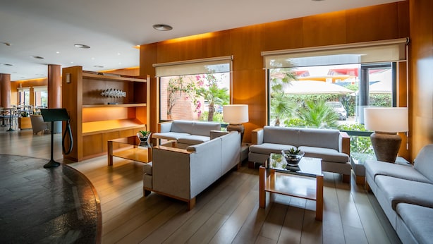 A modern hotel lobby with wooden paneling, comfortable seating, and large windows offering views of the outdoors.