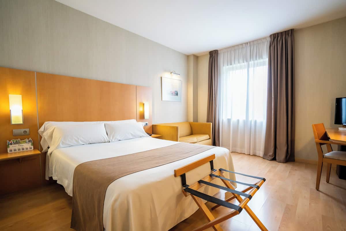 Ein Hotelzimmer mit einem Bett, einem Nachttisch aus Holz, einem Schreibtisch, einem Stuhl und einem Fernseher.