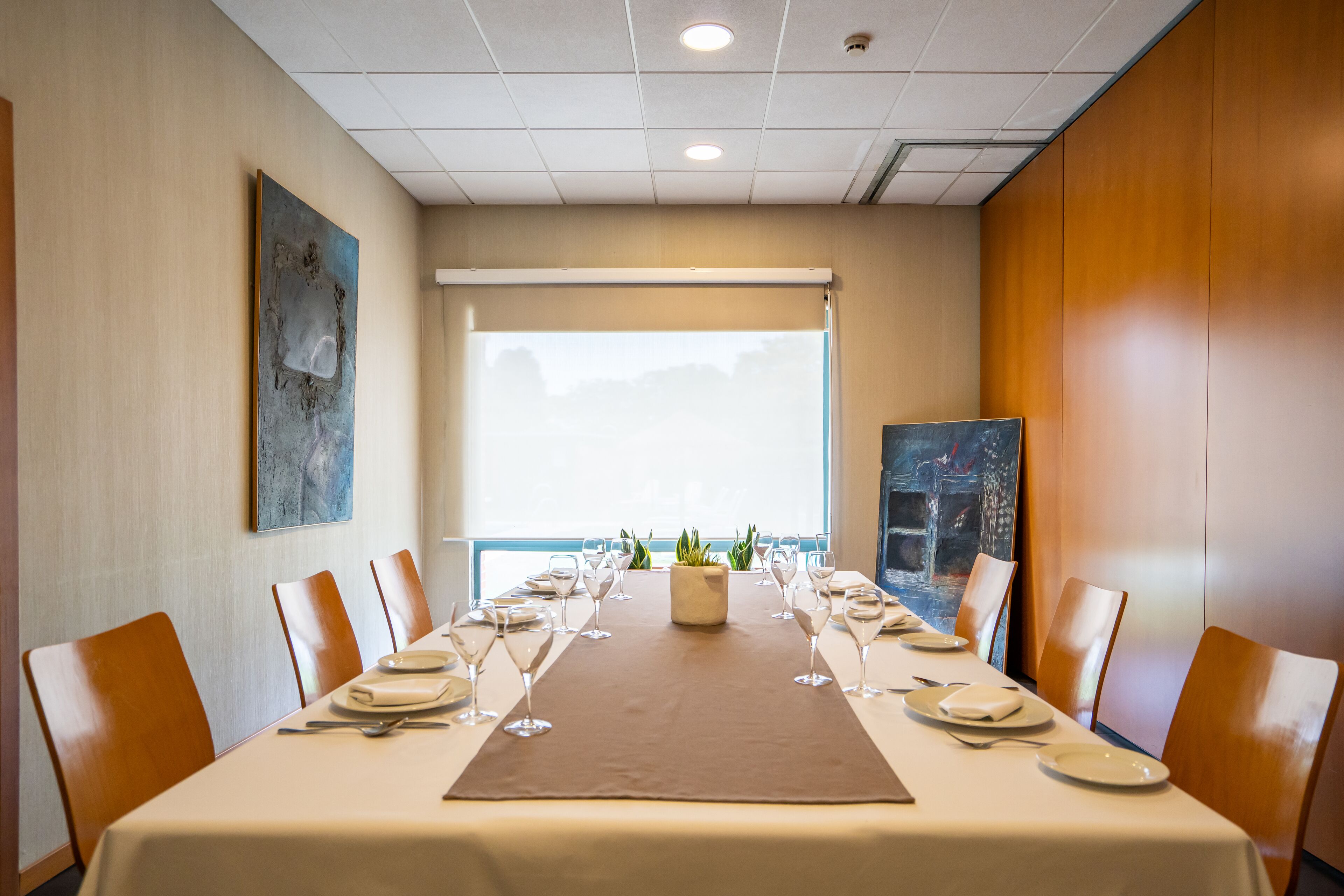 Une salle de conférence dotée d’une longue table préparée pour une réunion, entourée de chaises, avec une grande fenêtre et des œuvres d’art accrochées aux murs.