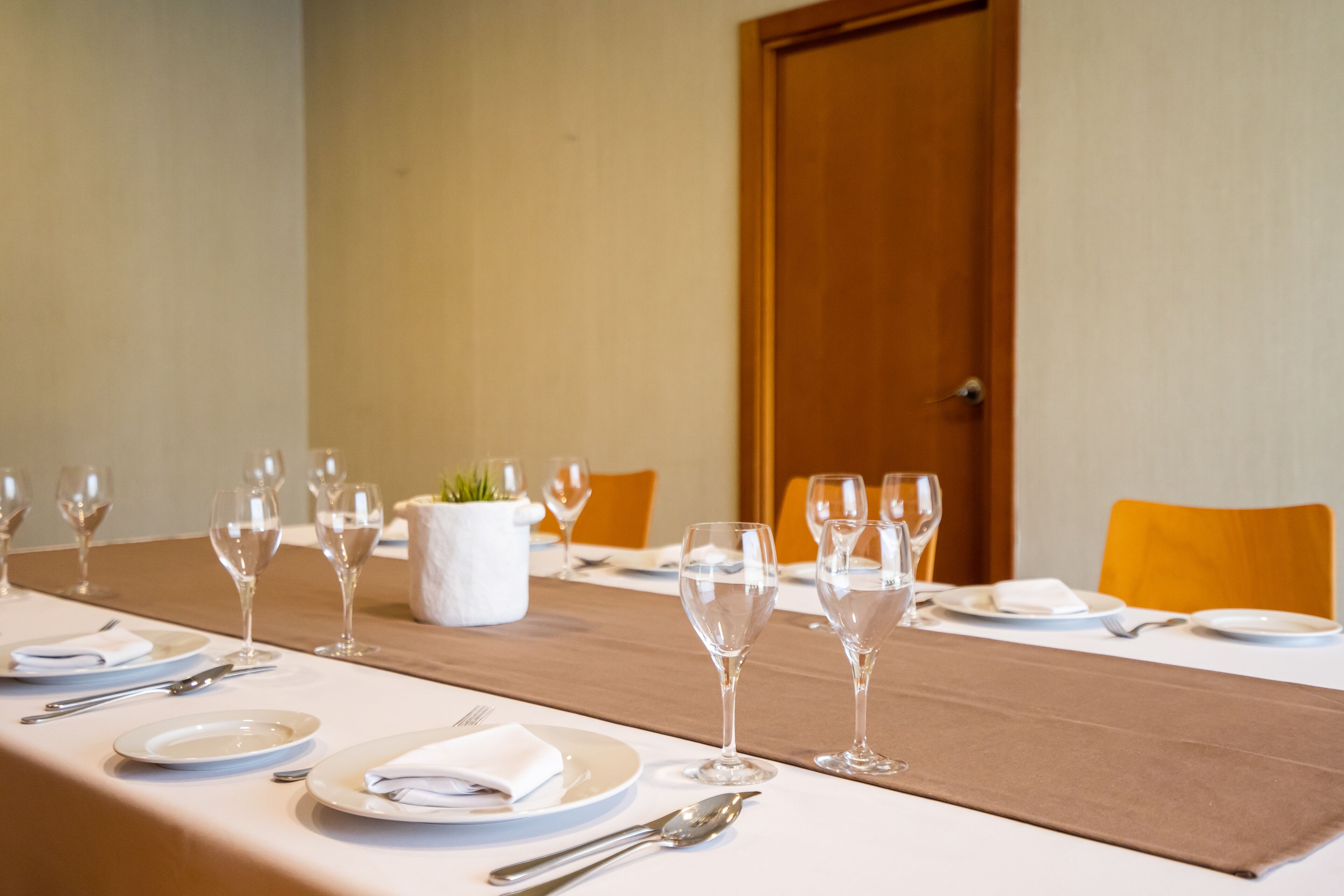 Una mesa de comedor lista para una comida, con platos, cubiertos y copas de vino.