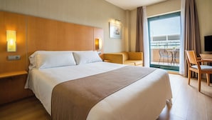 A hotel room with a large bed, a sofa, a desk, and a balcony with a view.
