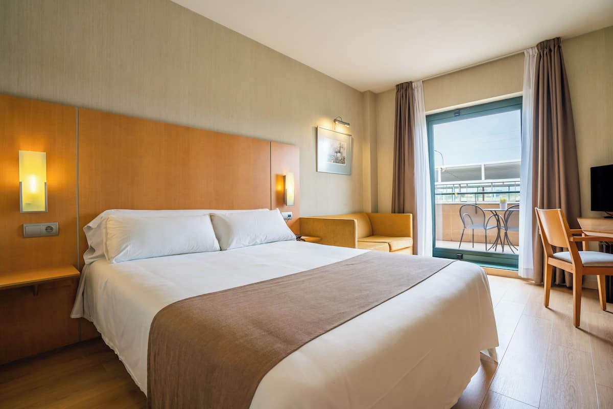 Ein Hotelzimmer mit einem großen Bett, einer Couch, einem Schreibtisch und einem Balkon mit Blick.