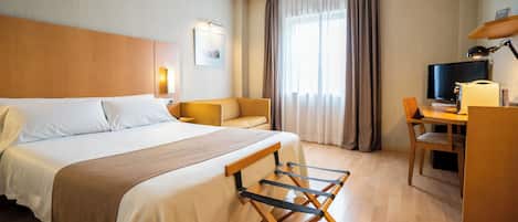 A hotel room with a large bed, a desk, a chair, a television, and a window with curtains.