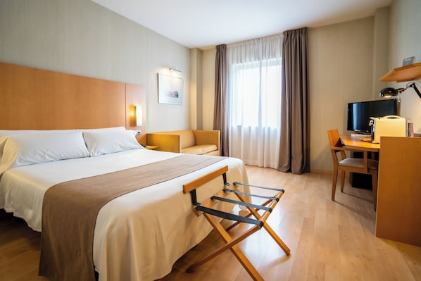 Habitación de hotel con una cama grande, un escritorio, una silla, un televisor y una ventana con cortinas.