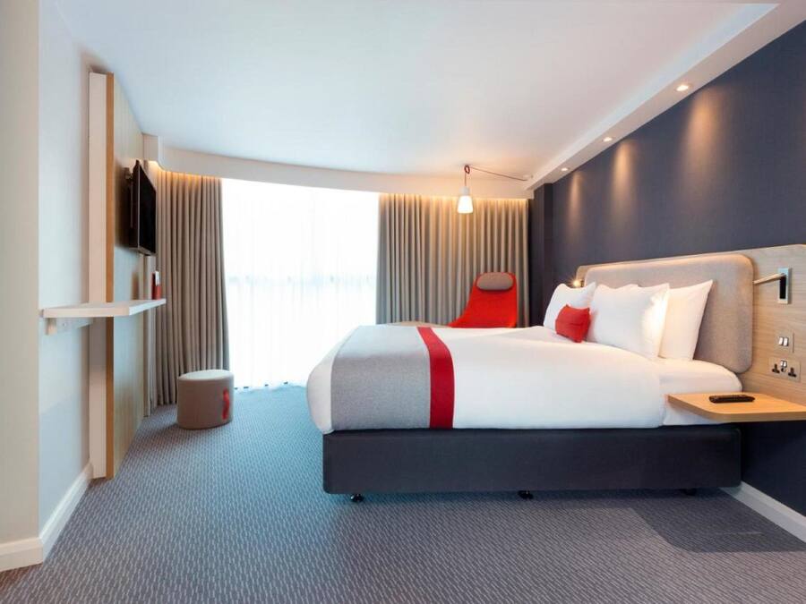 Una habitación de hotel moderna con una cama grande, un televisor montado en la pared y una ventana con cortinas.