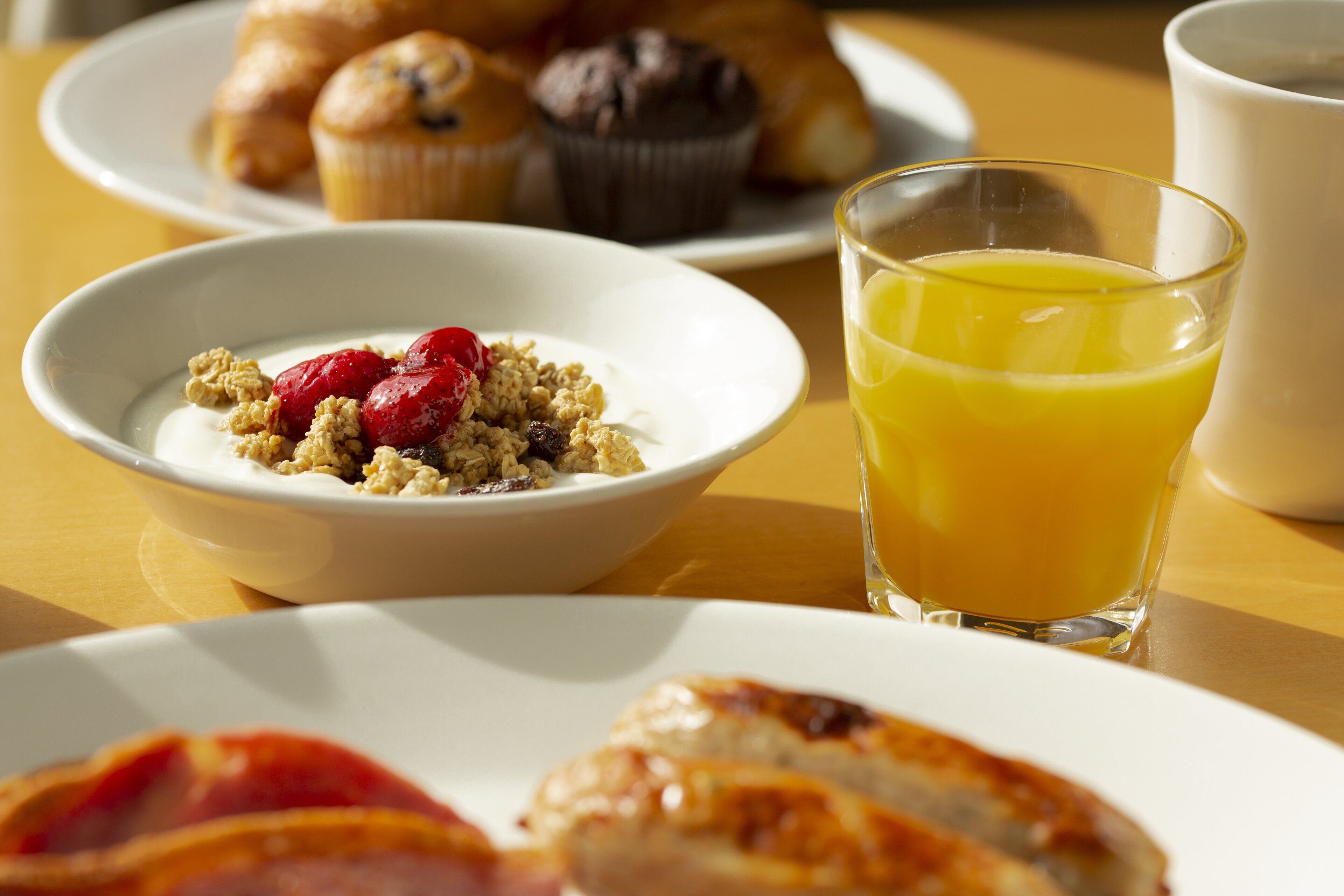 A breakfast setting with a bowl of cereal, a glass of orange juice, and croissants on a table.