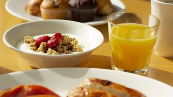 A breakfast setting with a bowl of cereal, a glass of orange juice, and croissants on a table.