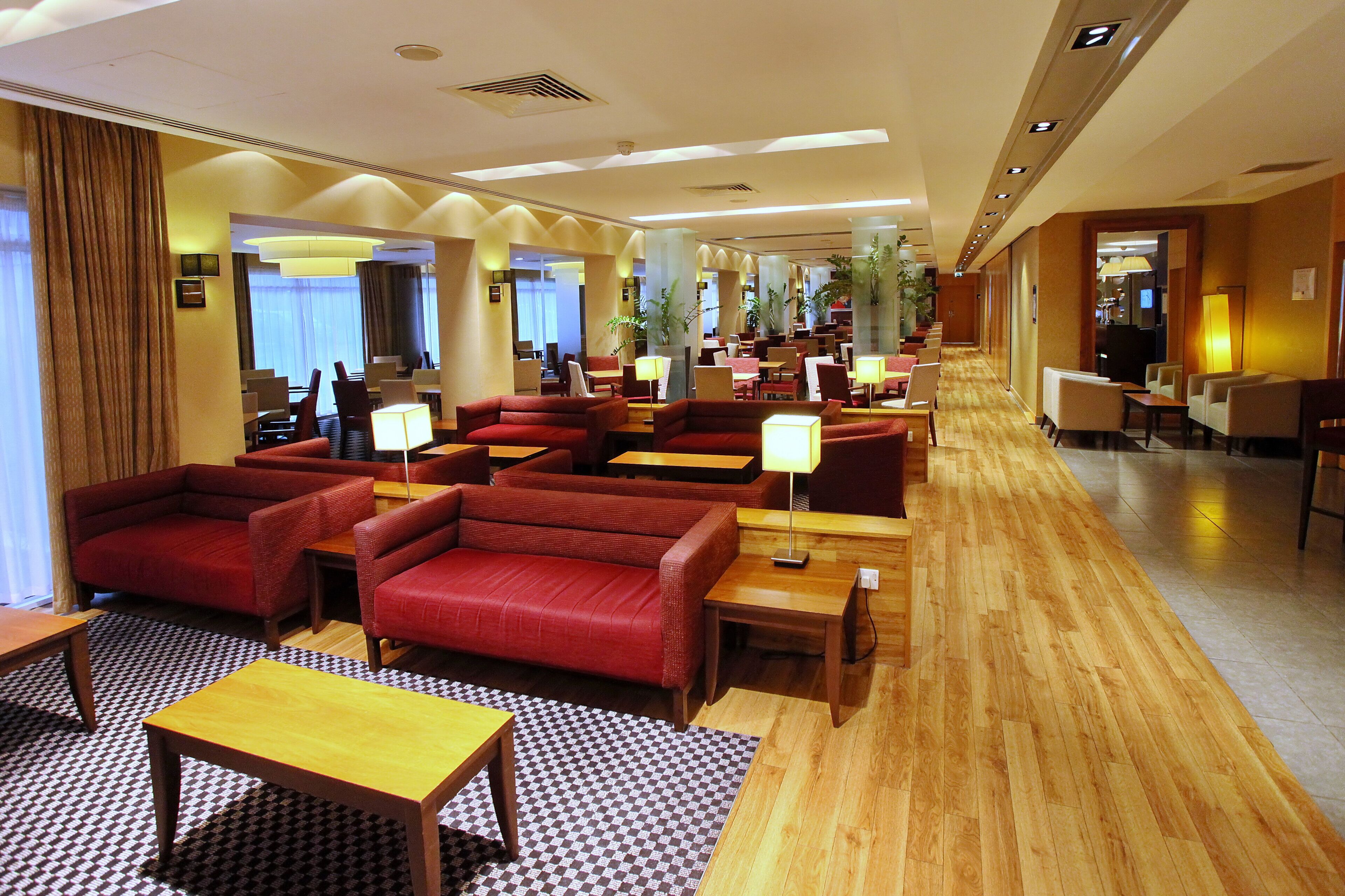 A hotel lobby with red seating, wooden tables, and a checkered floor pattern.