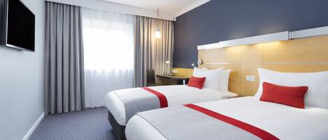Habitación de hotel con dos camas, televisión, escritorio y ventana con cortinas.