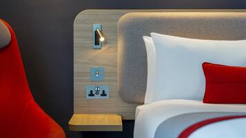 Une chambre d’hôtel moderne avec une tête de lit en bois, une table de chevet et une chaise rouge.