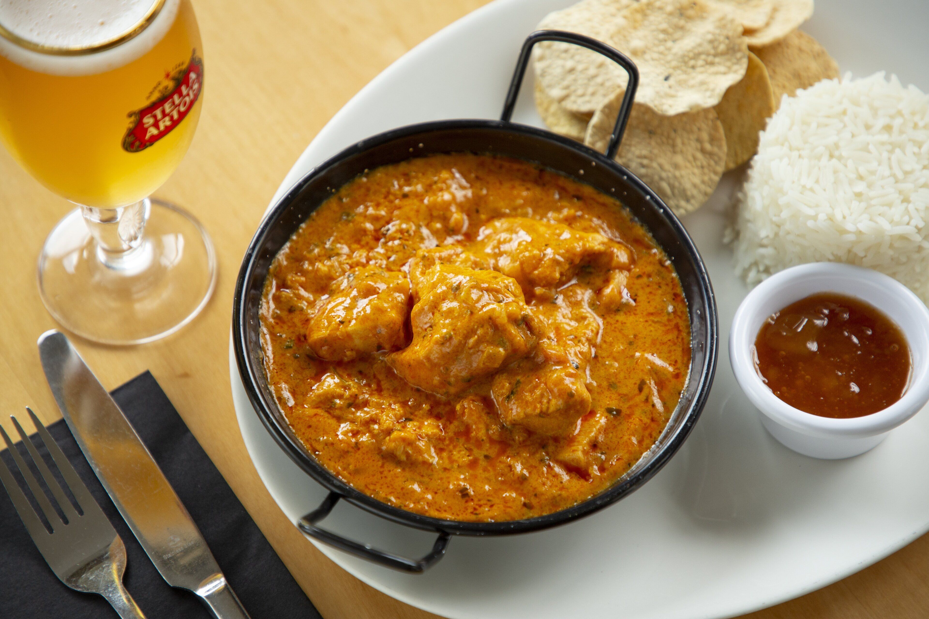 A meal consisting of a curry dish, rice, flatbread, and a glass of beer.