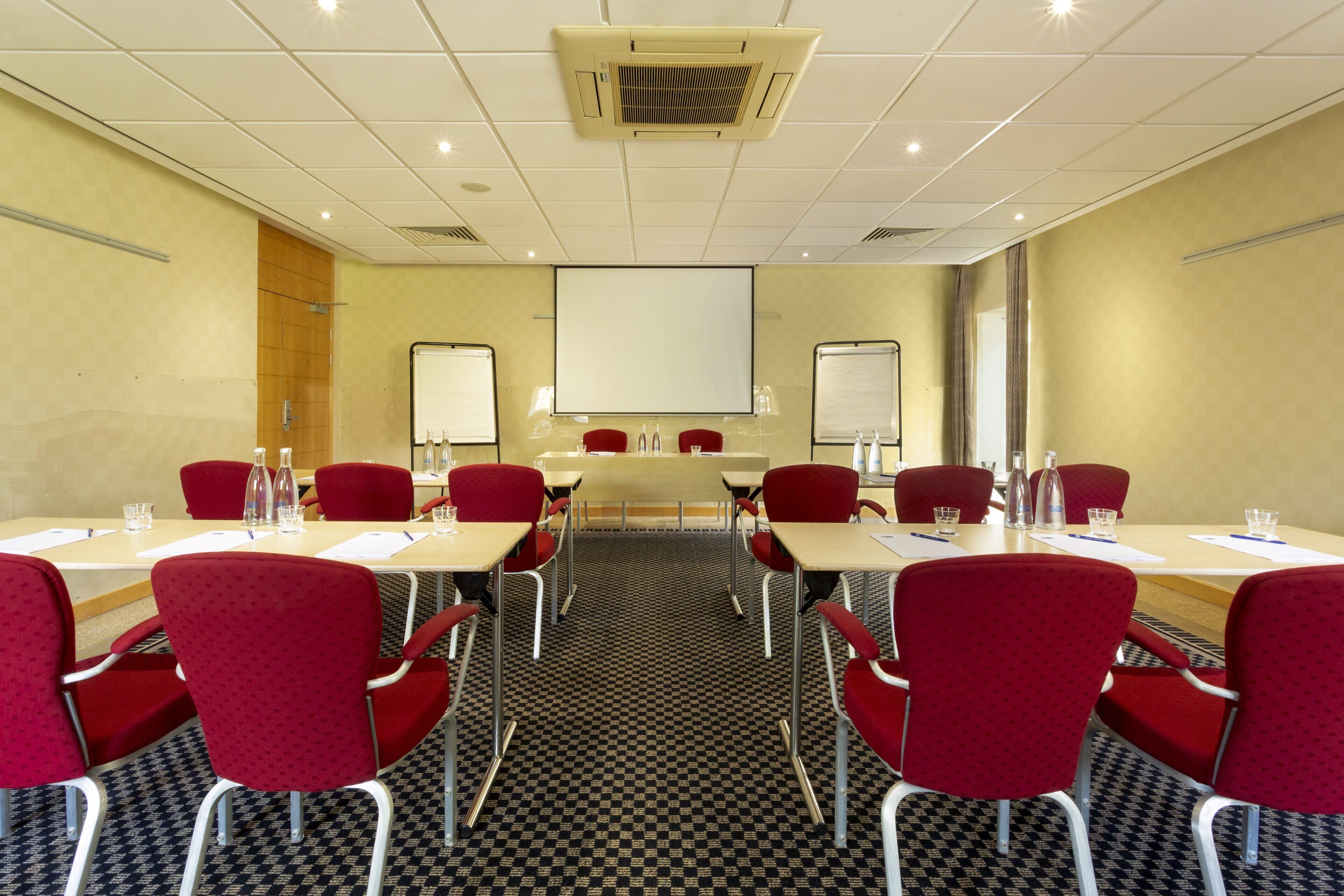 A conference room with a long table, red chairs, whiteboard screens, and a carpeted floor.