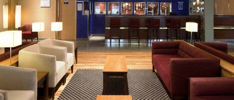 Un hall d’hôtel comprenant des espaces aménagés avec des sièges, un comptoir d’accueil et un bar.