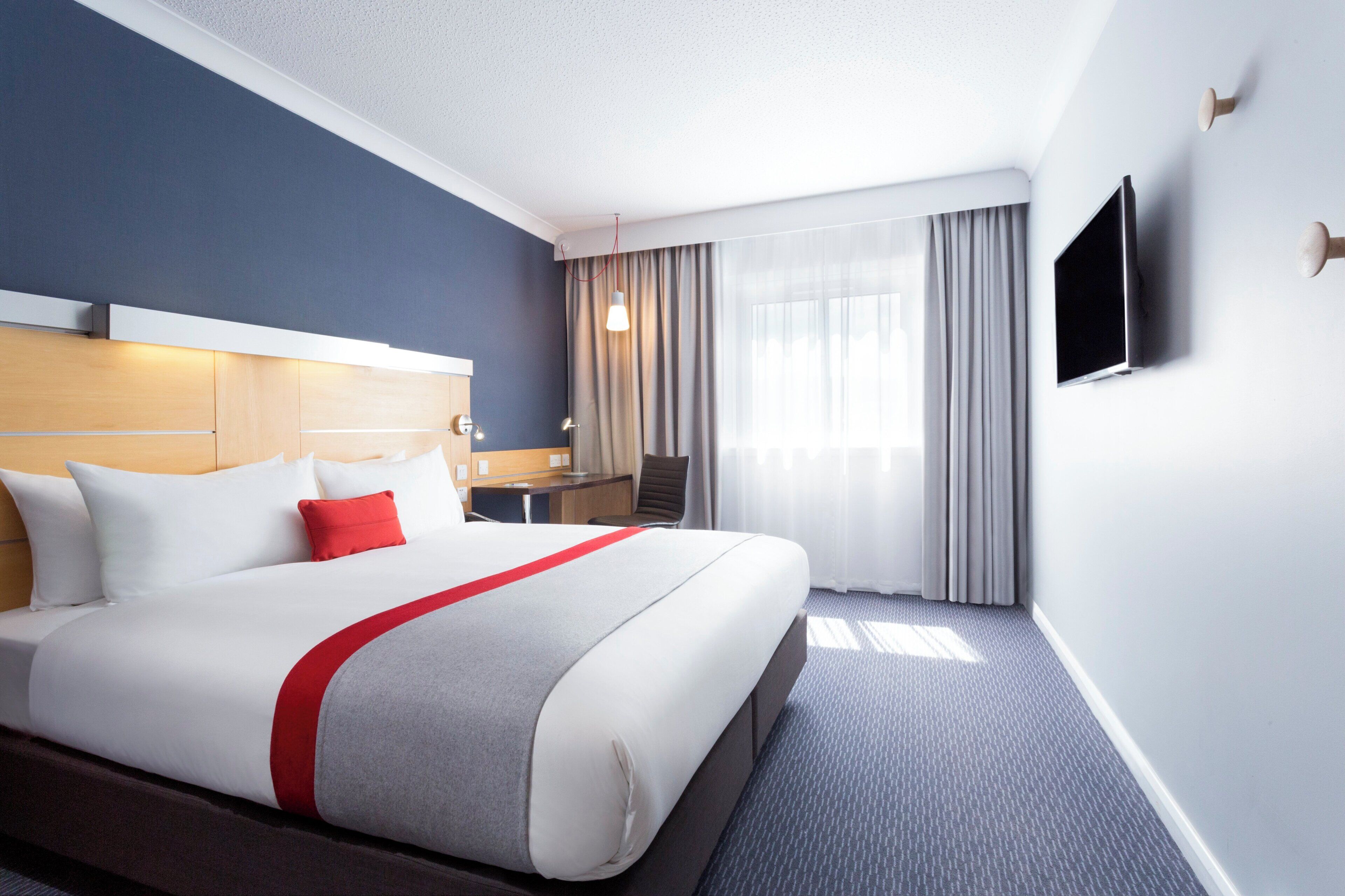 Una habitación de hotel con una cama grande, un escritorio, una silla, un televisor y una ventana con cortinas.