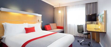 A hotel room with a large bed, a desk with a chair, a television, and a window with curtains.