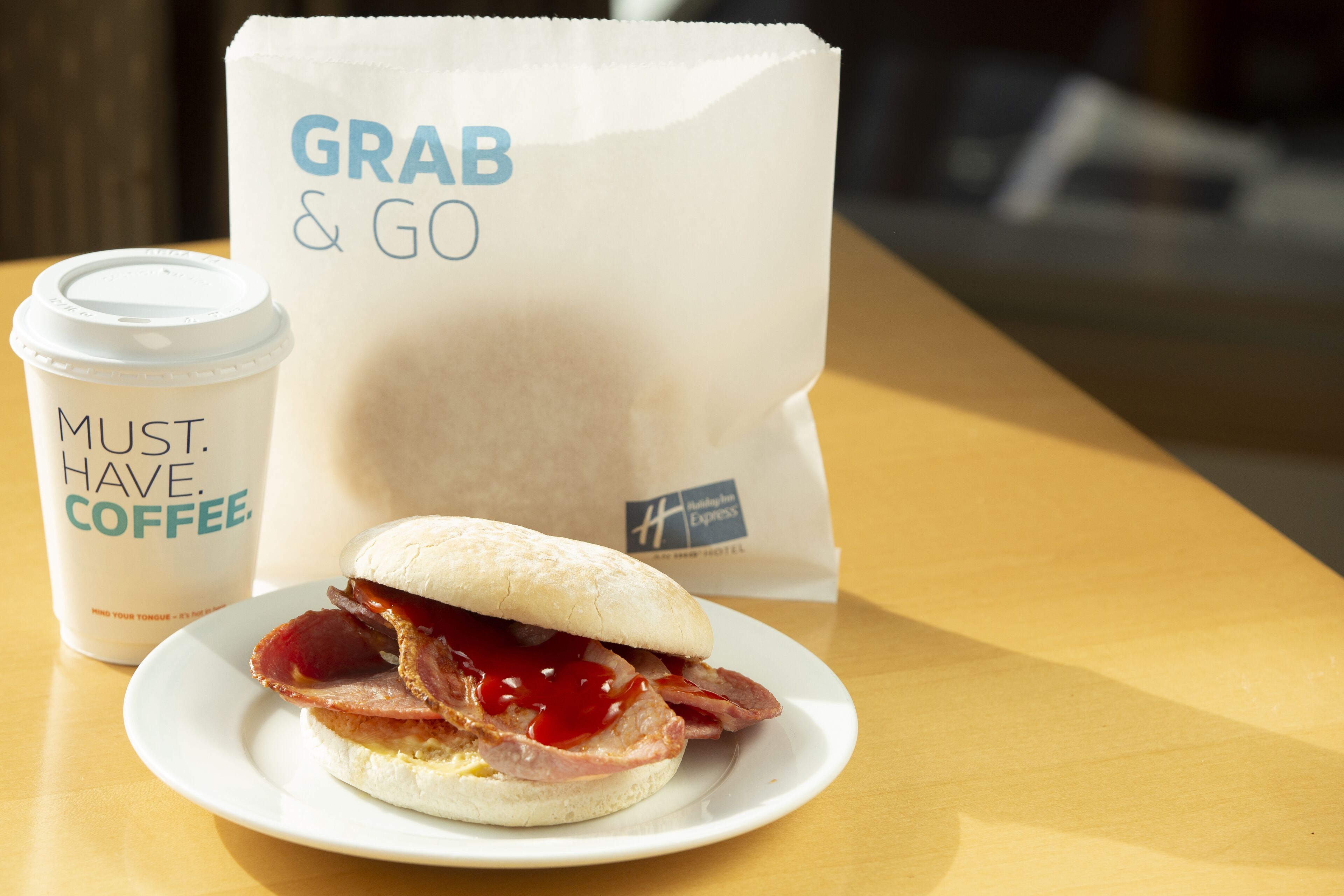 A sandwich on a plate, a coffee cup, and a paper bag with "GRAB & GO" written on it.