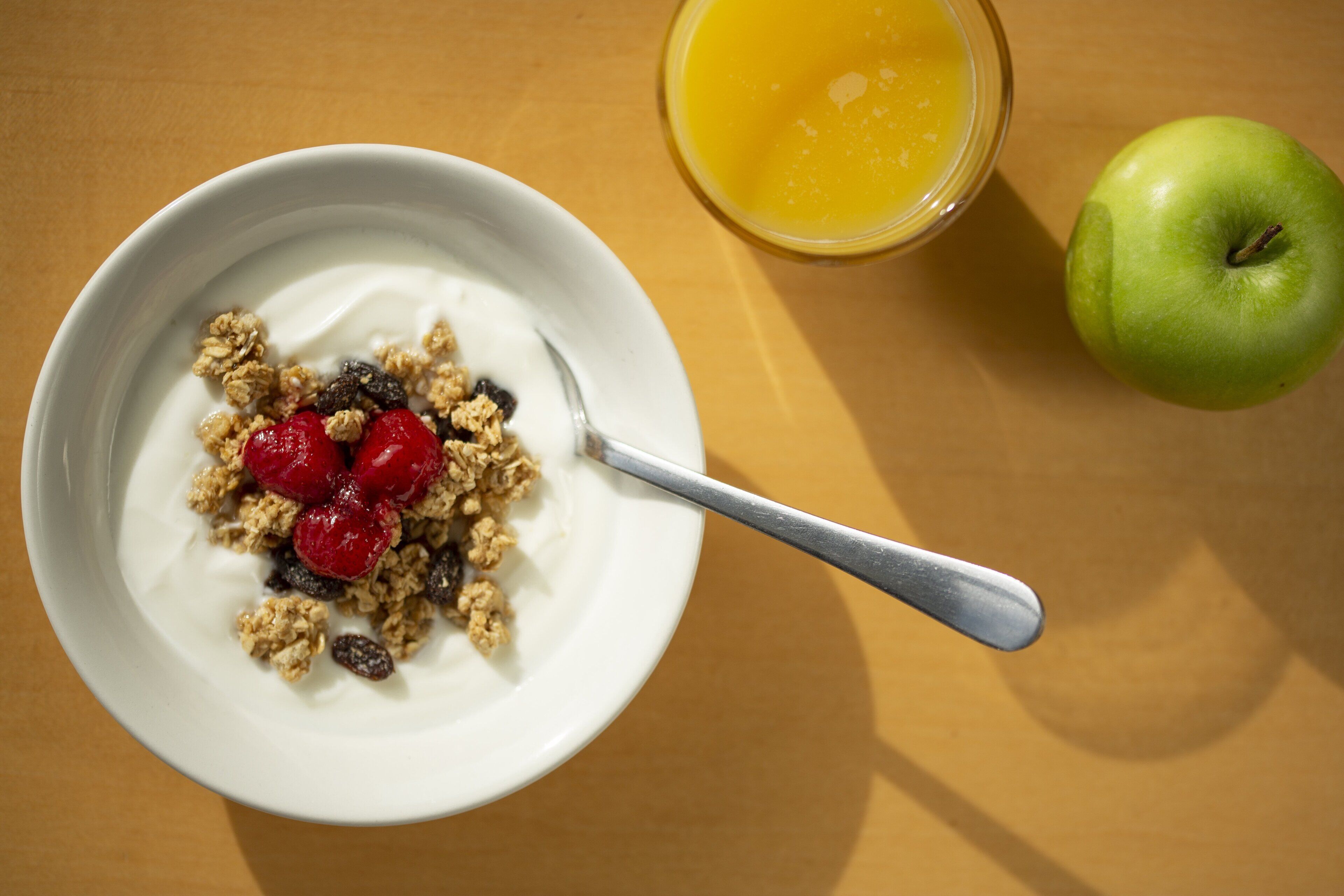 A bowl of cereal with milk and fruit, a glass of orange juice, and an apple on a table.