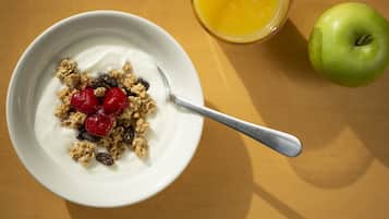 A bowl of cereal with milk and fruit, a glass of orange juice, and an apple on a table.