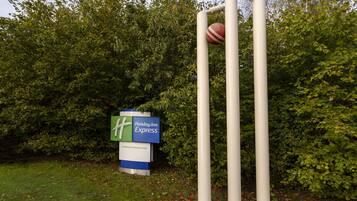 Un campo de cricket con tocones y pelota, y un cartel de Holiday Inn Express al fondo.