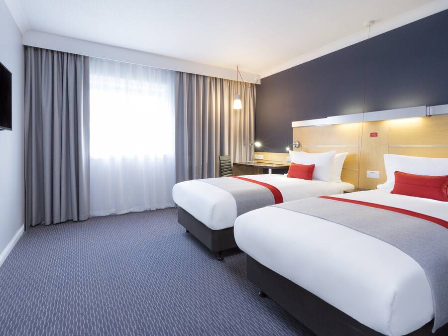 A hotel room with two beds, a flat-screen TV, a desk, and a window with curtains.